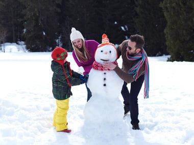 happy young  family playing in fresh snow and making snowman at beautiful sunny winter day outdoor in nature with forest in background